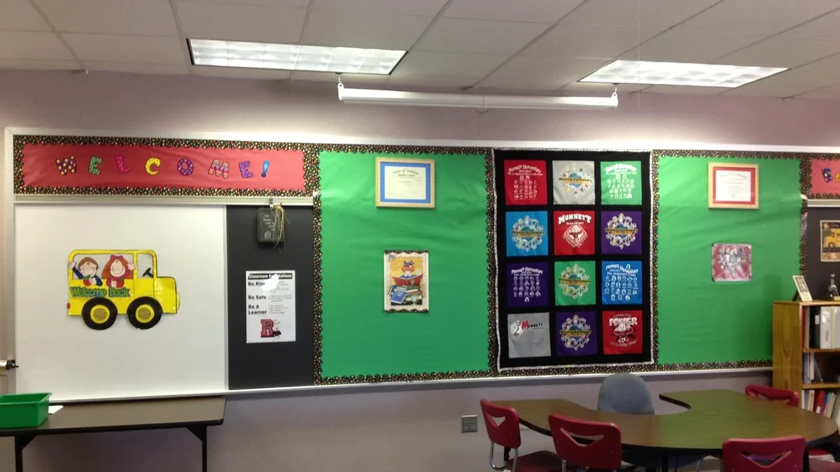 A classroom with a bulletin board, a whiteboard, and a table with chairs.